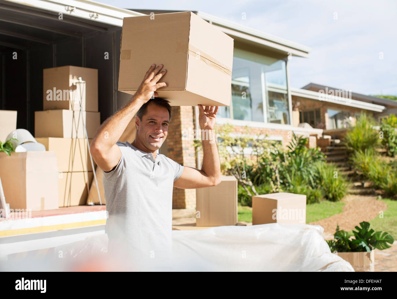 Man holding cardboard box overhead near moving van in driveway Stock Photo