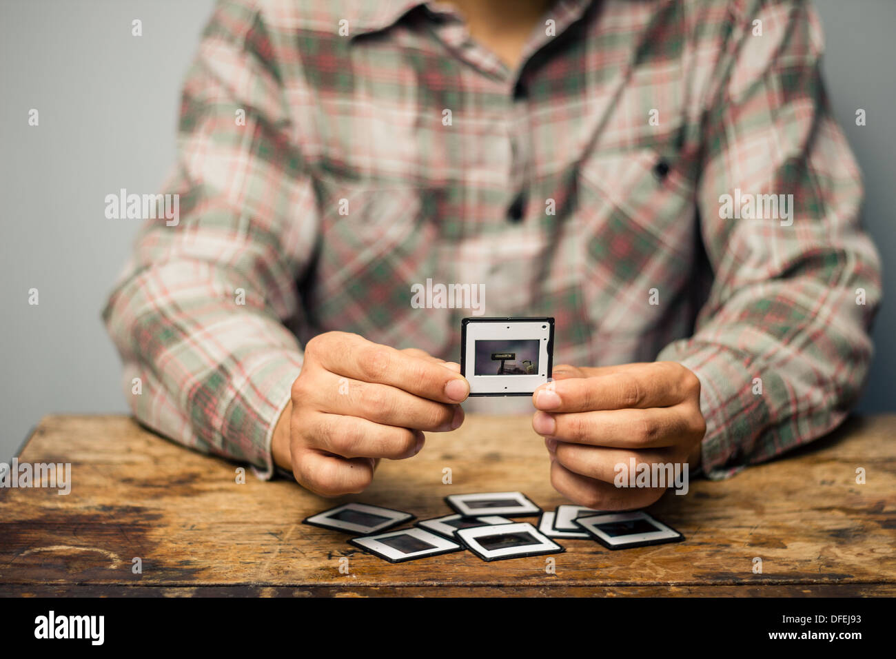 Young man is sitting at a table and looking over his old slides Stock Photo