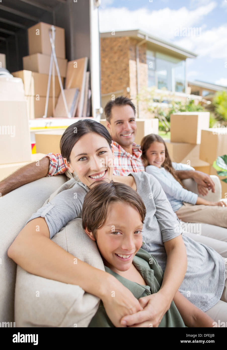 Family sitting on sofa near moving van in driveway Stock Photo