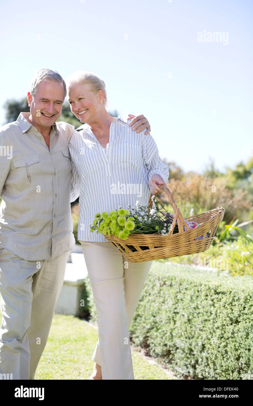 Senior couple walking in garden with basket of flowers Stock Photo
