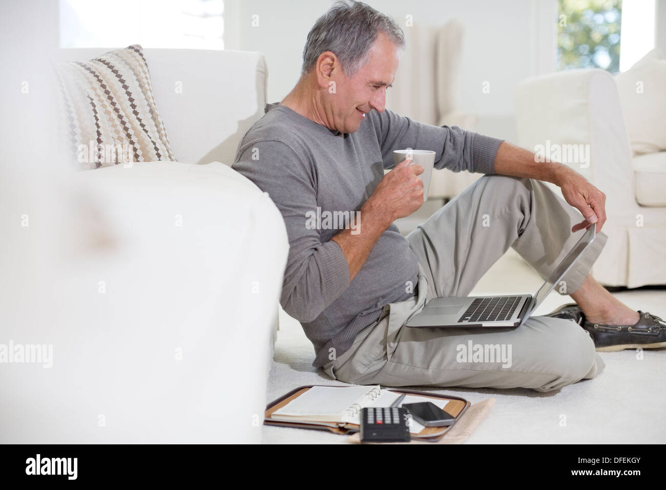 Senior man using laptop on living room floor Stock Photo