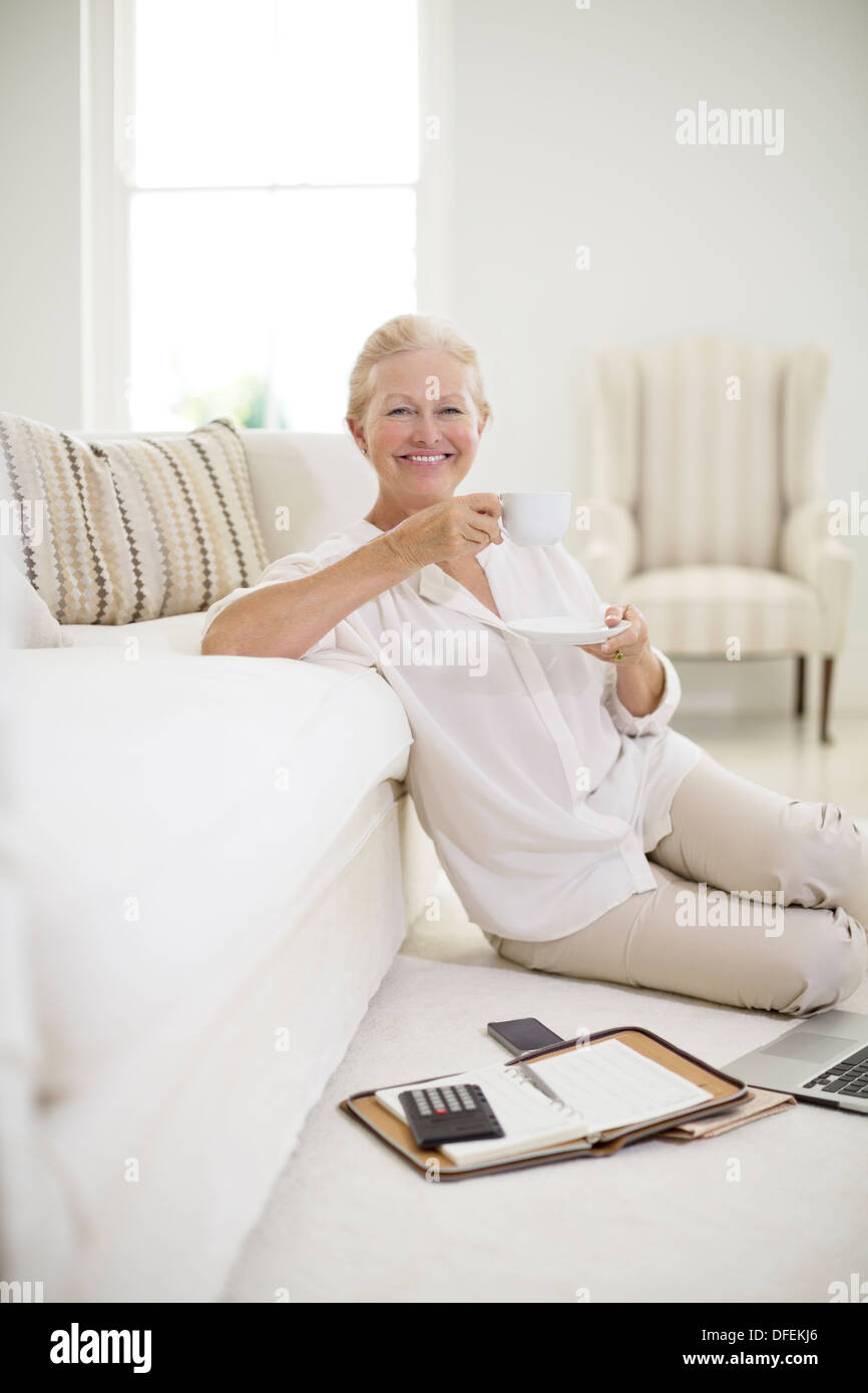 Senior woman drinking coffee on living room floor Stock Photo