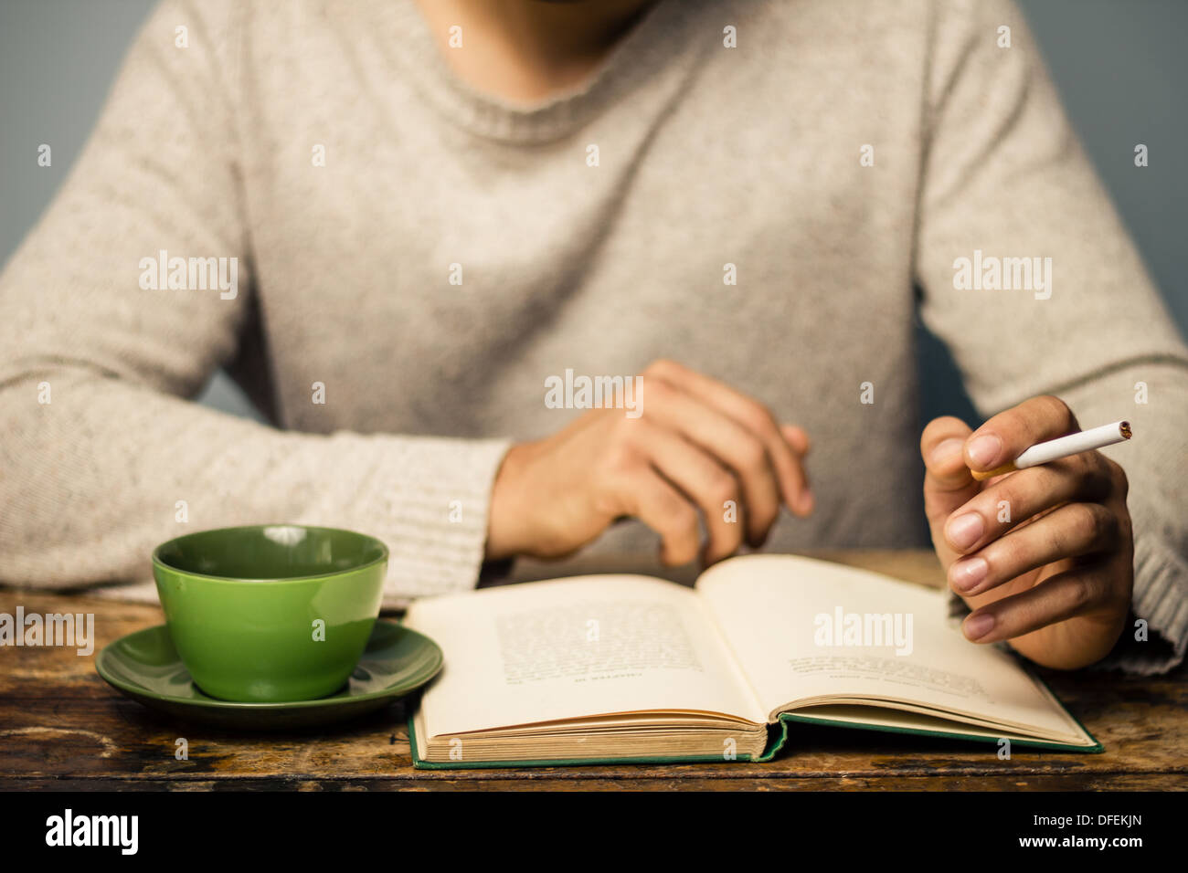 Man is reading, drinking coffee and smoking a cigarette at table Stock  Photo