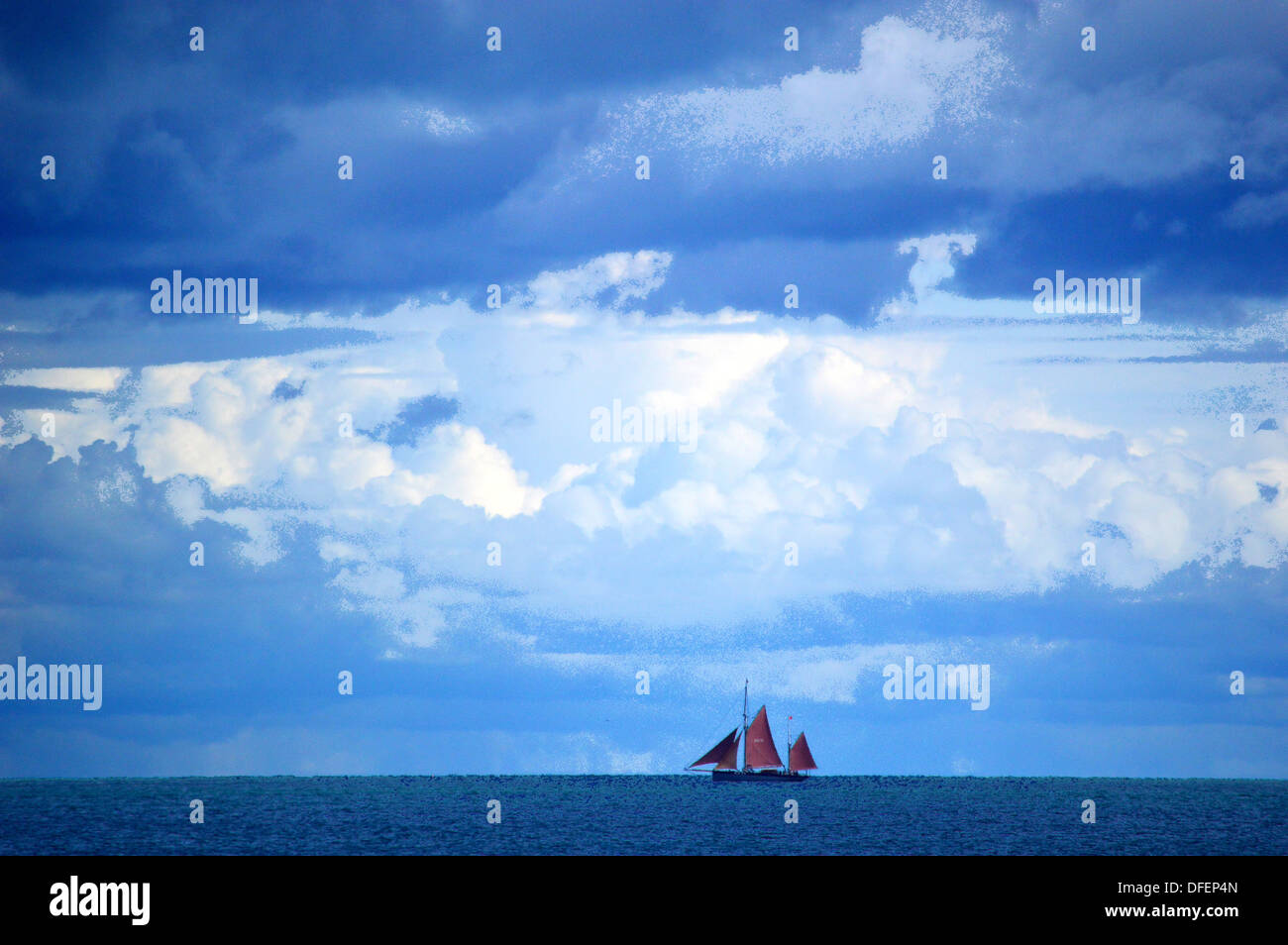 Red sails of ship on horizon with stormy clouded sky Stock Photo
