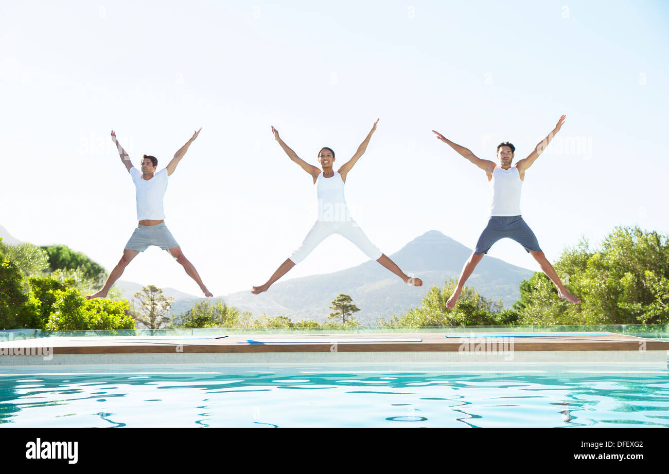 People jumping with arms and legs outstretched at poolside Stock Photo