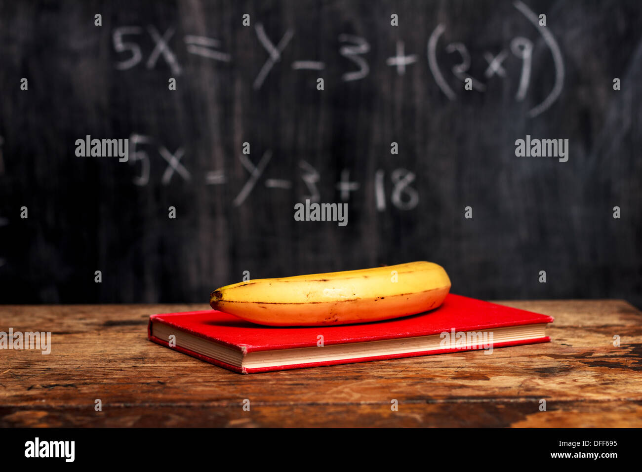 Book and banana on desk in front of blackboard with math problem Stock Photo