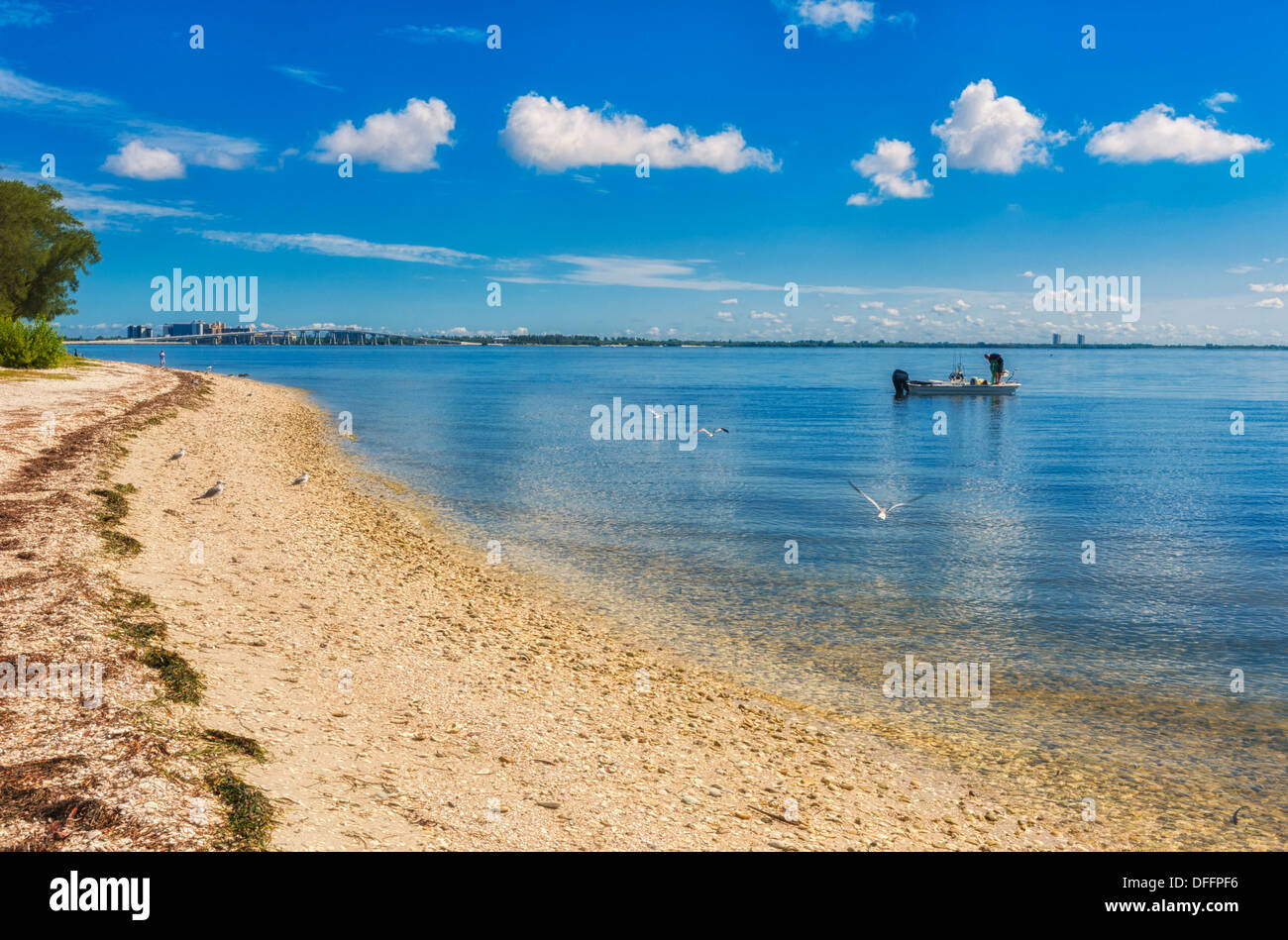 Two men fish at a distance near the coast in summer blue sky and ocean. Causeway in background. Stock Photo