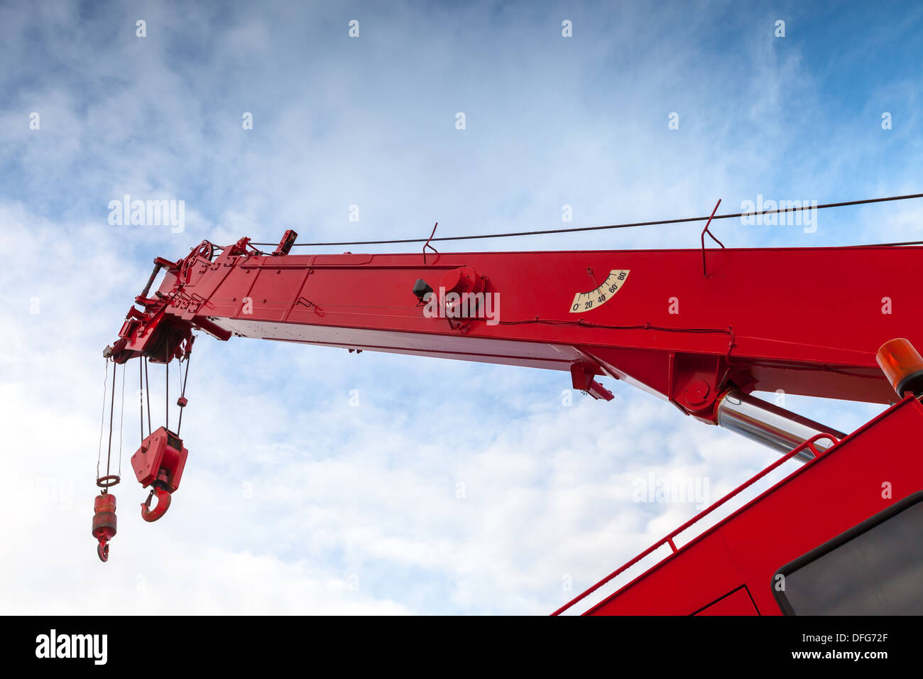 Red truck crane boom with hooks and scale weight above blue sky Stock Photo