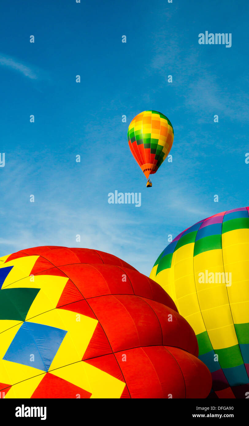 A colorful hot air balloon flies in a bright blue sky as two more are inflated on the ground. Stock Photo