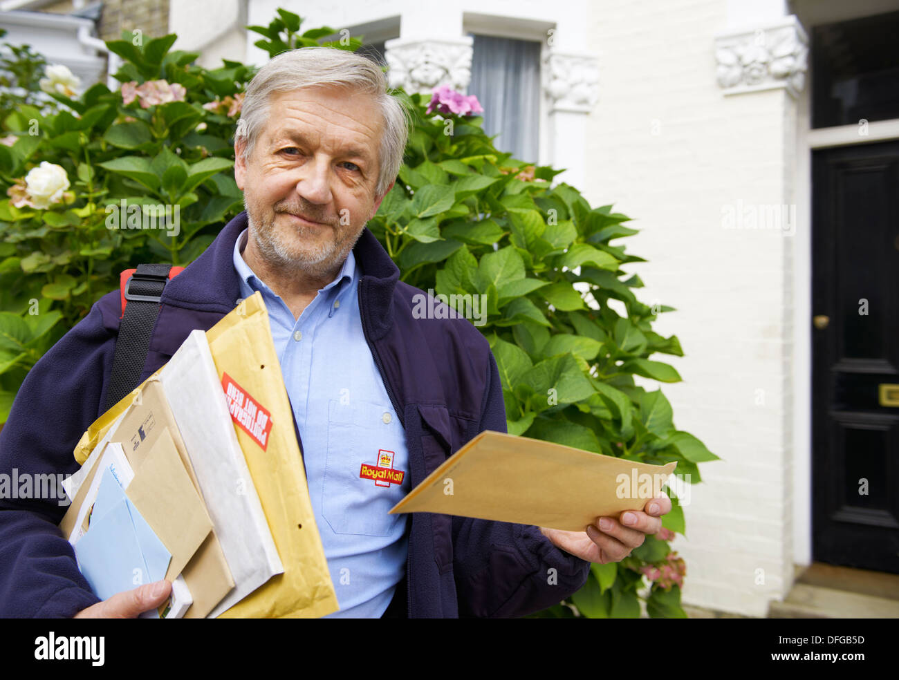 Royal Mail Postman routinely delivering letters, airmail, packages and parcels in residential area in the UK Stock Photo