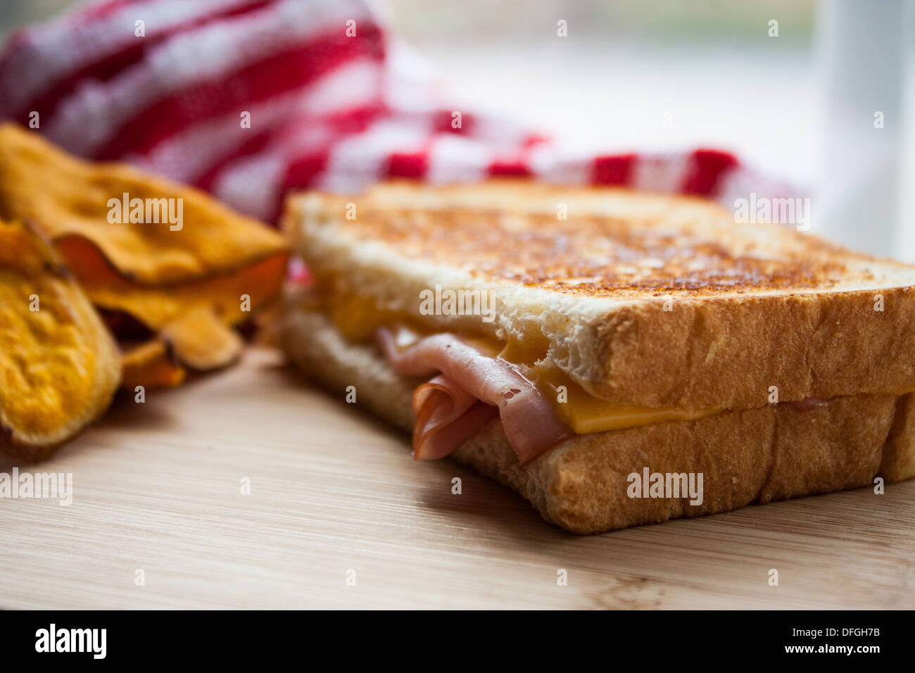 Grilled ham and cheese sandwich on a wooden cutting board with sweet potato chips. Stock Photo