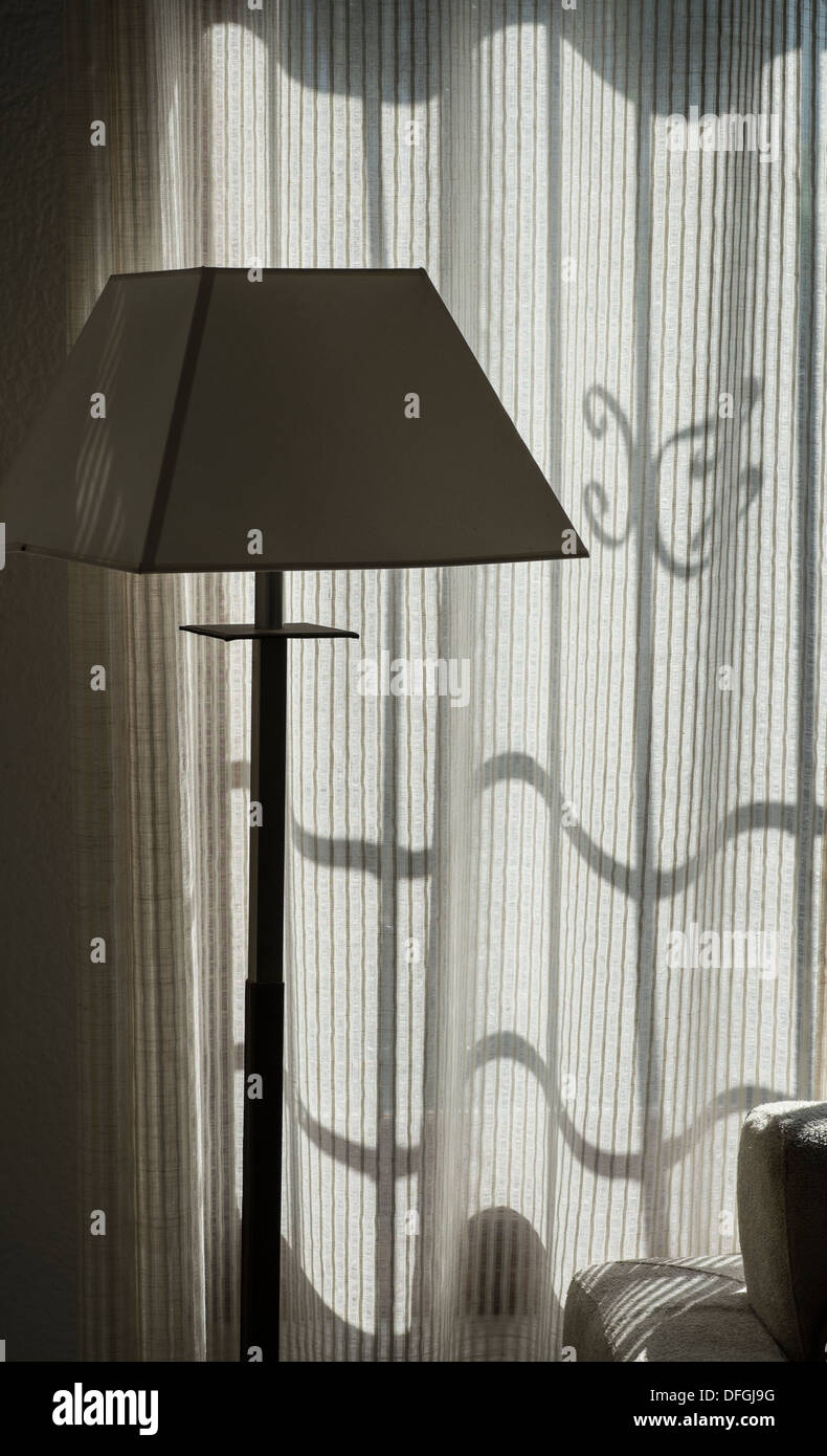 Light and shade in a Spanish villa window.  A standard lamp with shadows of window security bars on a curtain. Stock Photo