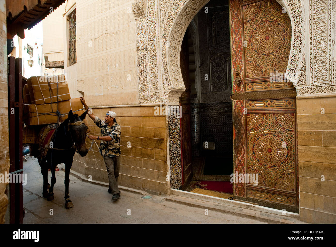 Horse carrying goods in a street of the 'medina' ( old town). At the right, one of the entrance of the Sidi Ahmed Tijani mosque. Stock Photo