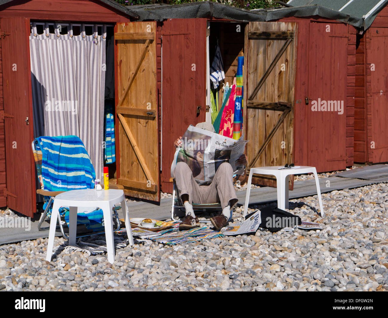 Man reading newspaper beside beach huts at Beer Devon England UK Stock Photo