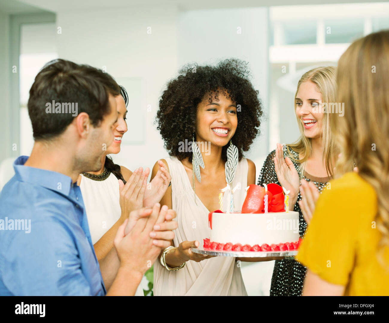 Friends clapping around woman with birthday cake Stock Photo