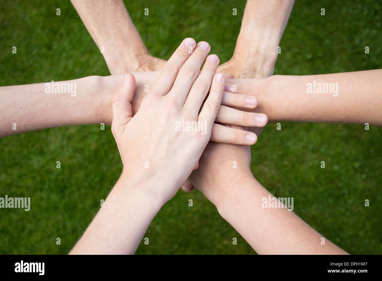 Six arms on top of each other uniting above grass Stock Photo