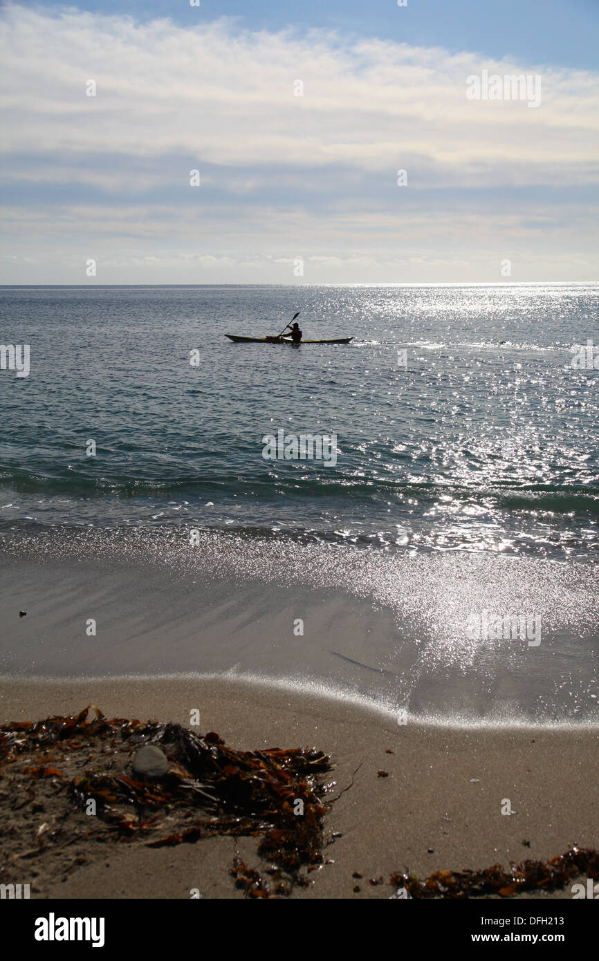 Seaside view of man in kayak off the beach with sunlight glistening on the water Stock Photo