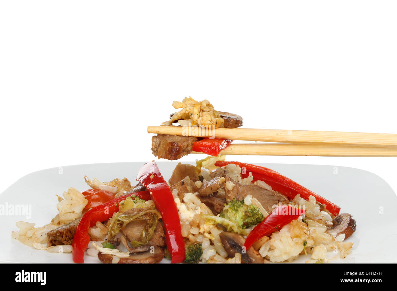 Beef and vegetable stir fry with chopsticks above a plate against a white background Stock Photo