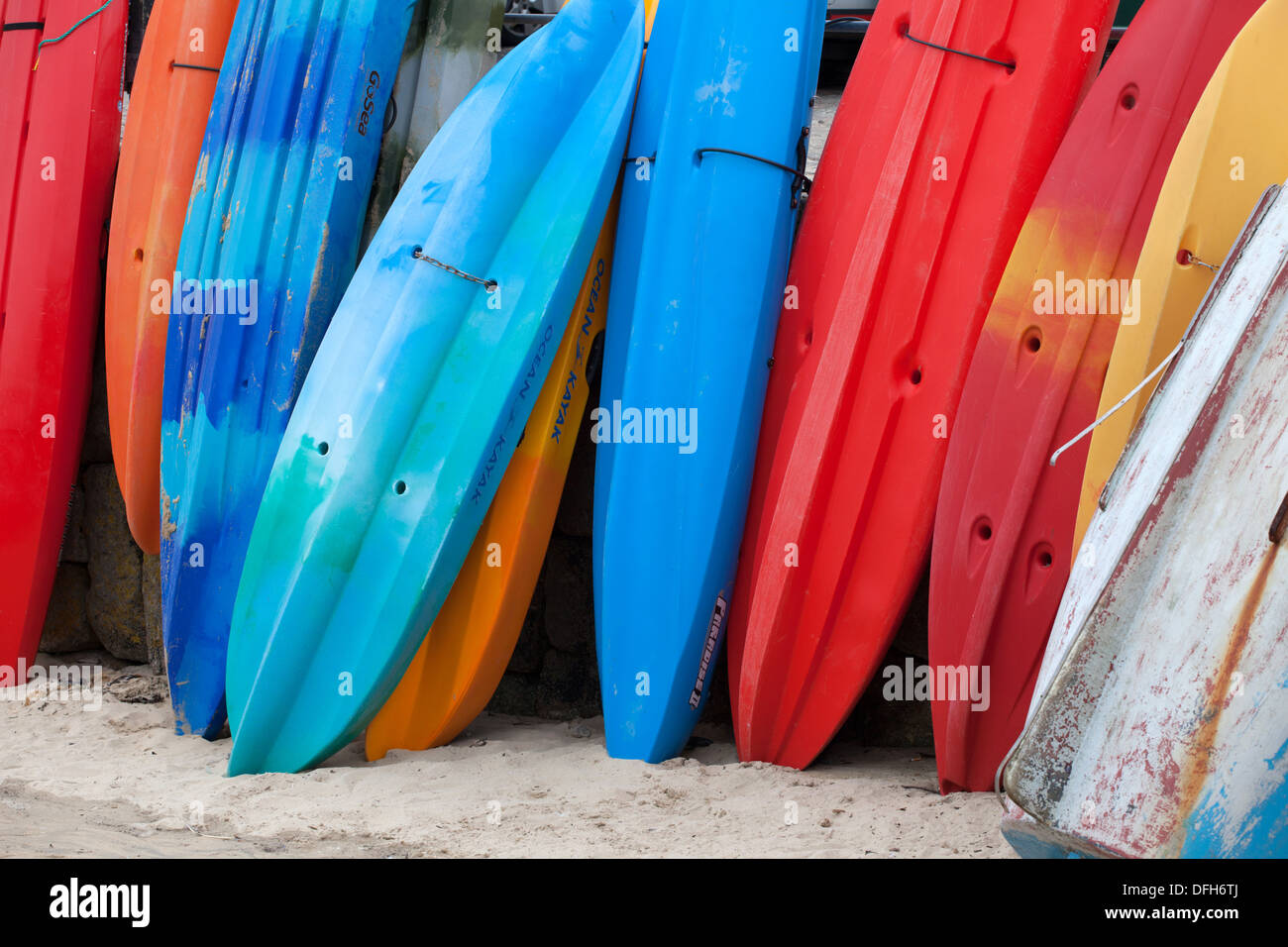 Colourful kayaks stacked up against the harbour wall, Mousehole Cornwall Stock Photo