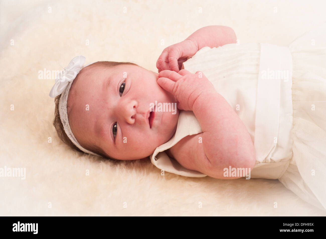 Newborn baby girl with white hair band in cream coloured dress Stock Photo