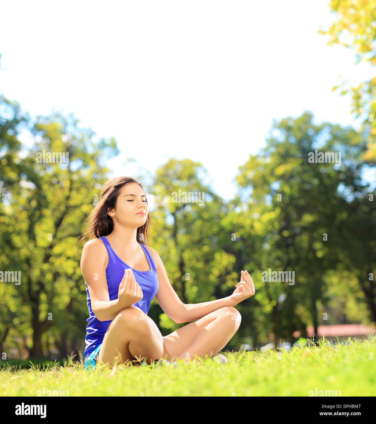 Young female athlete in sportswear meditating seated on a green grass in a park Stock Photo