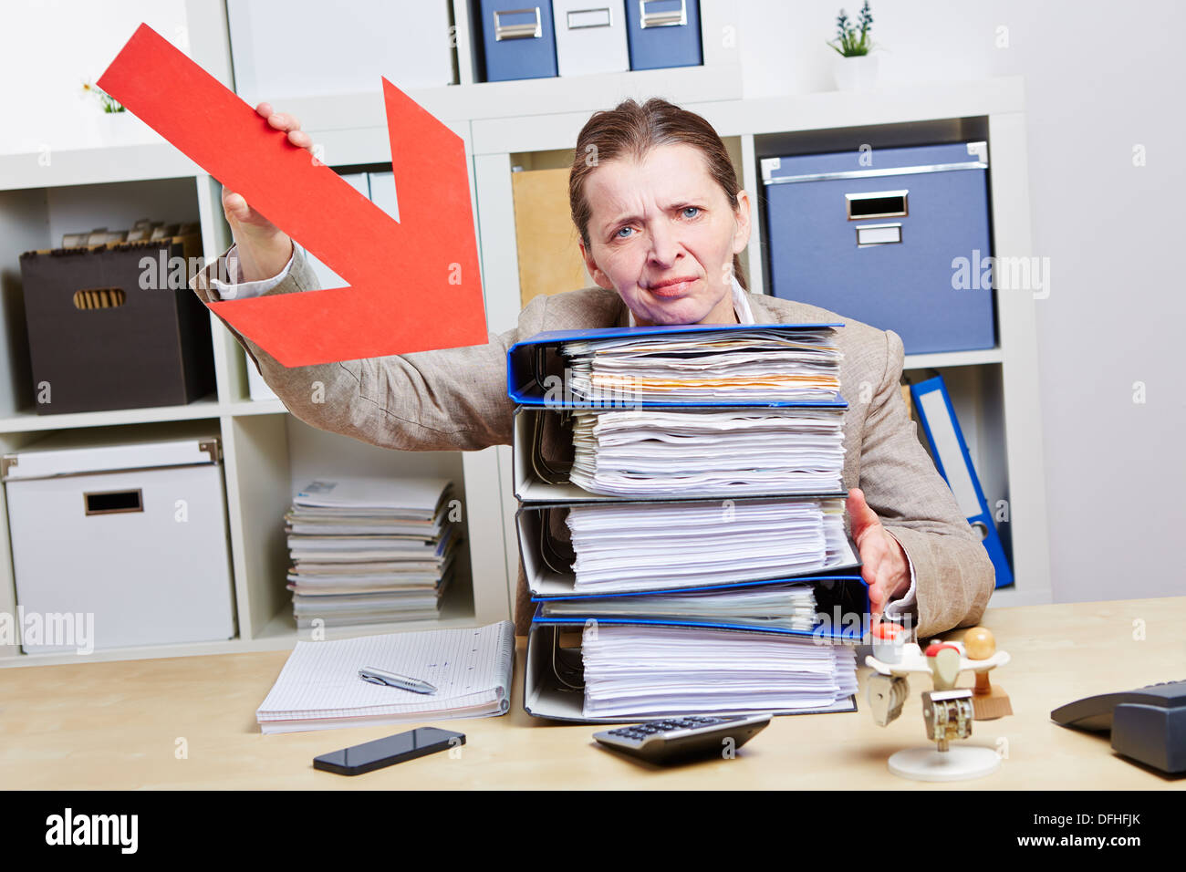 Business woman with burnout pointing arrow to files in her office Stock Photo