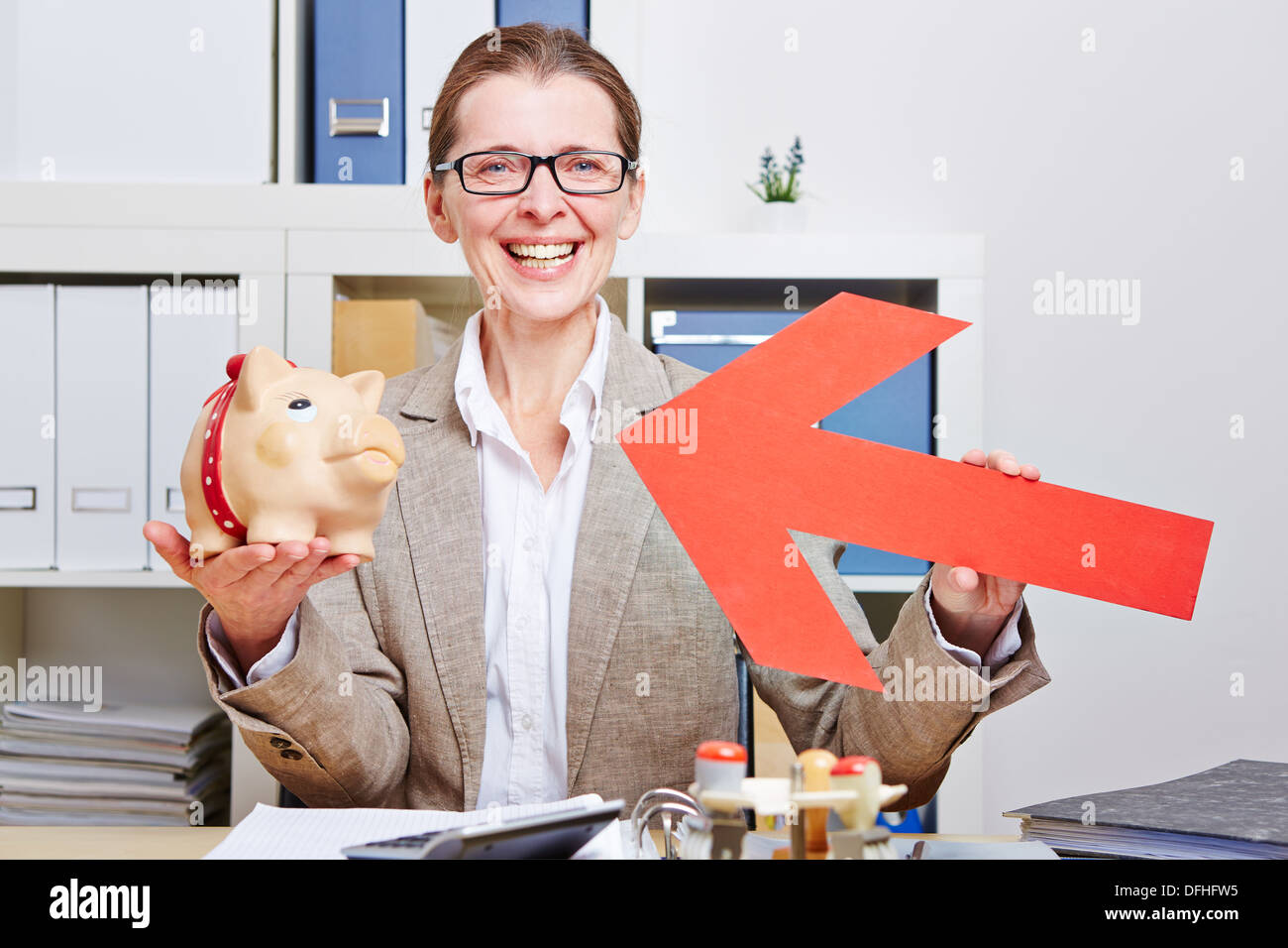 Happy senior business woman pointing red arrow to piggy bank in her ...