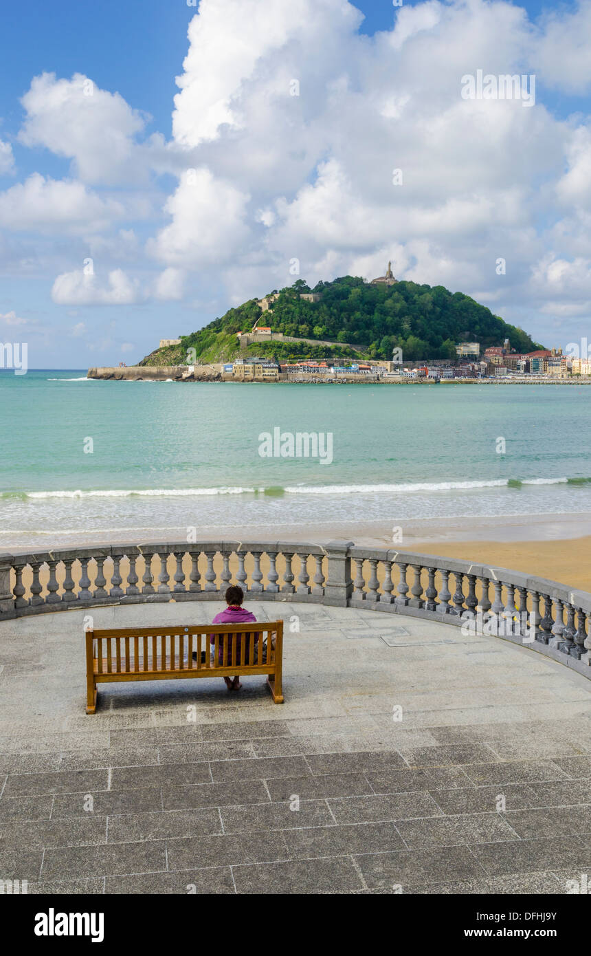 Woman seated on a bench on the Promenade La Concha overlooking the beach and Monte Urgull, San Sebastian, Spain Stock Photo
