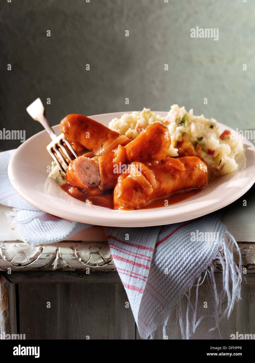 Traditional cooked Sausage and mash served on a white plate in a table setting ready to eat Stock Photo
