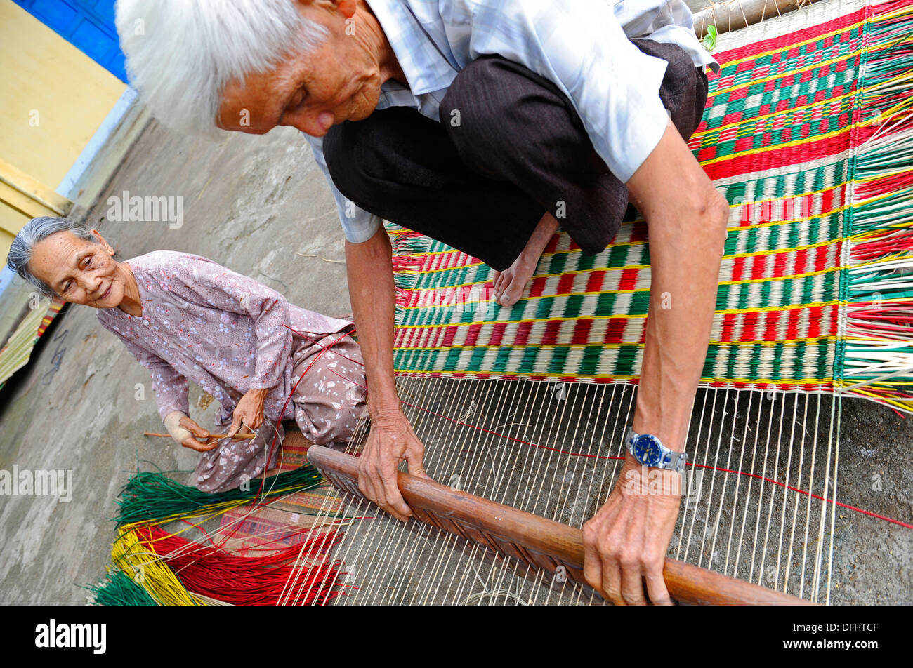 Elderly Vietnamese hand making colourful reed floor mats Stock Photo