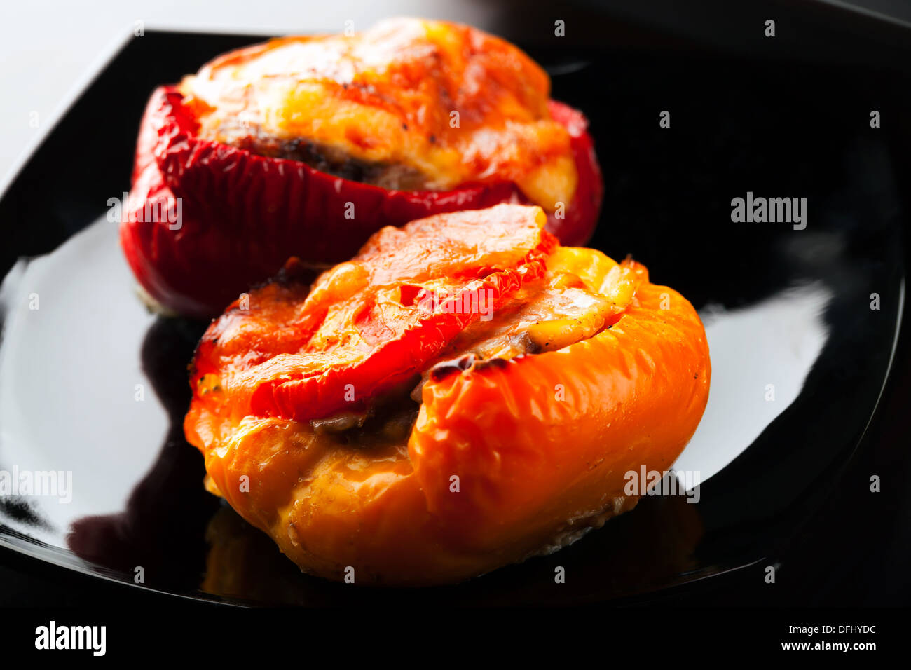 Stuffed bell peppers with chopped meat, cheese and tomato lay on black plate Stock Photo