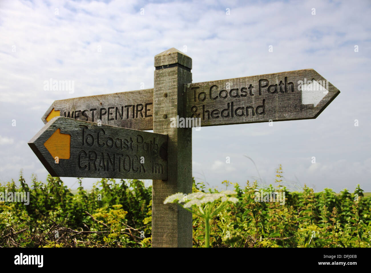 A coastal path wooden finger post with yellow arrows and a misspelt ...