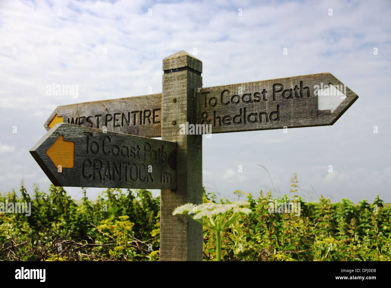 A coastal path wooden finger post with yellow arrows and a misspelt word 'headland' Stock Photo