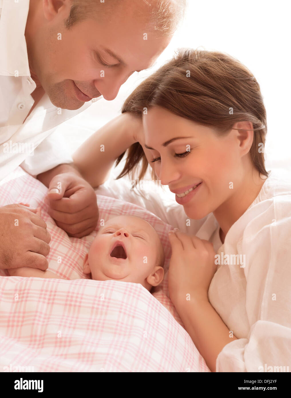 Newborn baby awake, parents looking on child, loving family, mother and father with little daughter on the bed at home Stock Photo