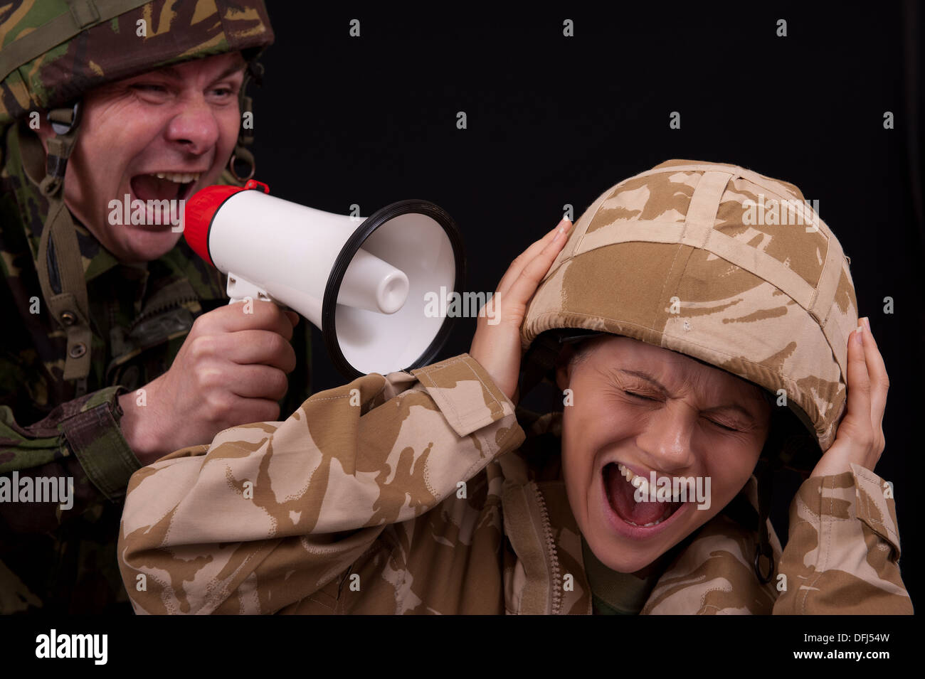 Male soldier shouting orders to a distraught female soldier with the use of a small hand held loudspeaker. British uniforms. Stock Photo