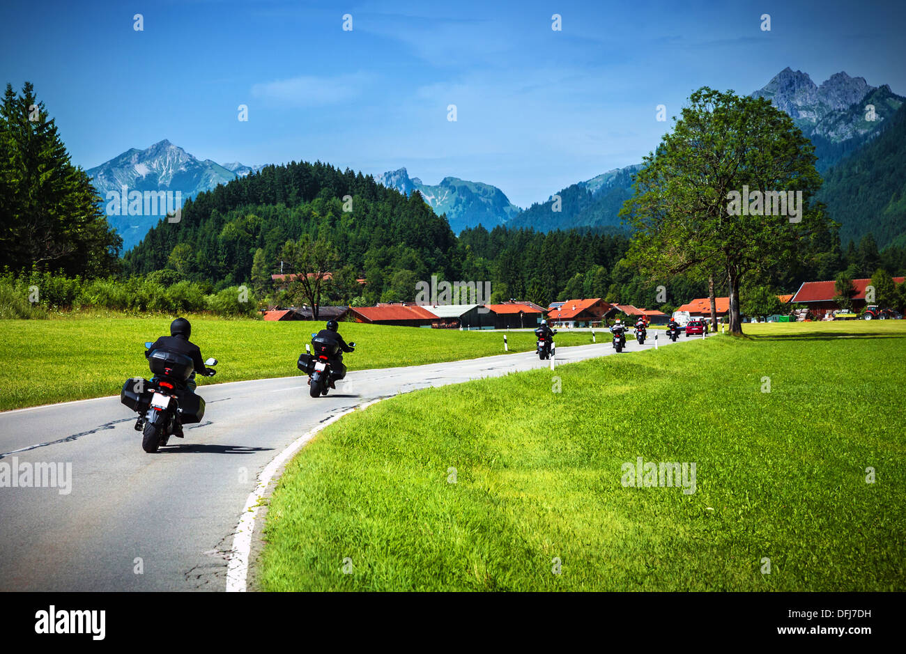 Bikers on mountainous road, touring across Alpine mountains, along little village, beautiful landscape, travel and tourism Stock Photo