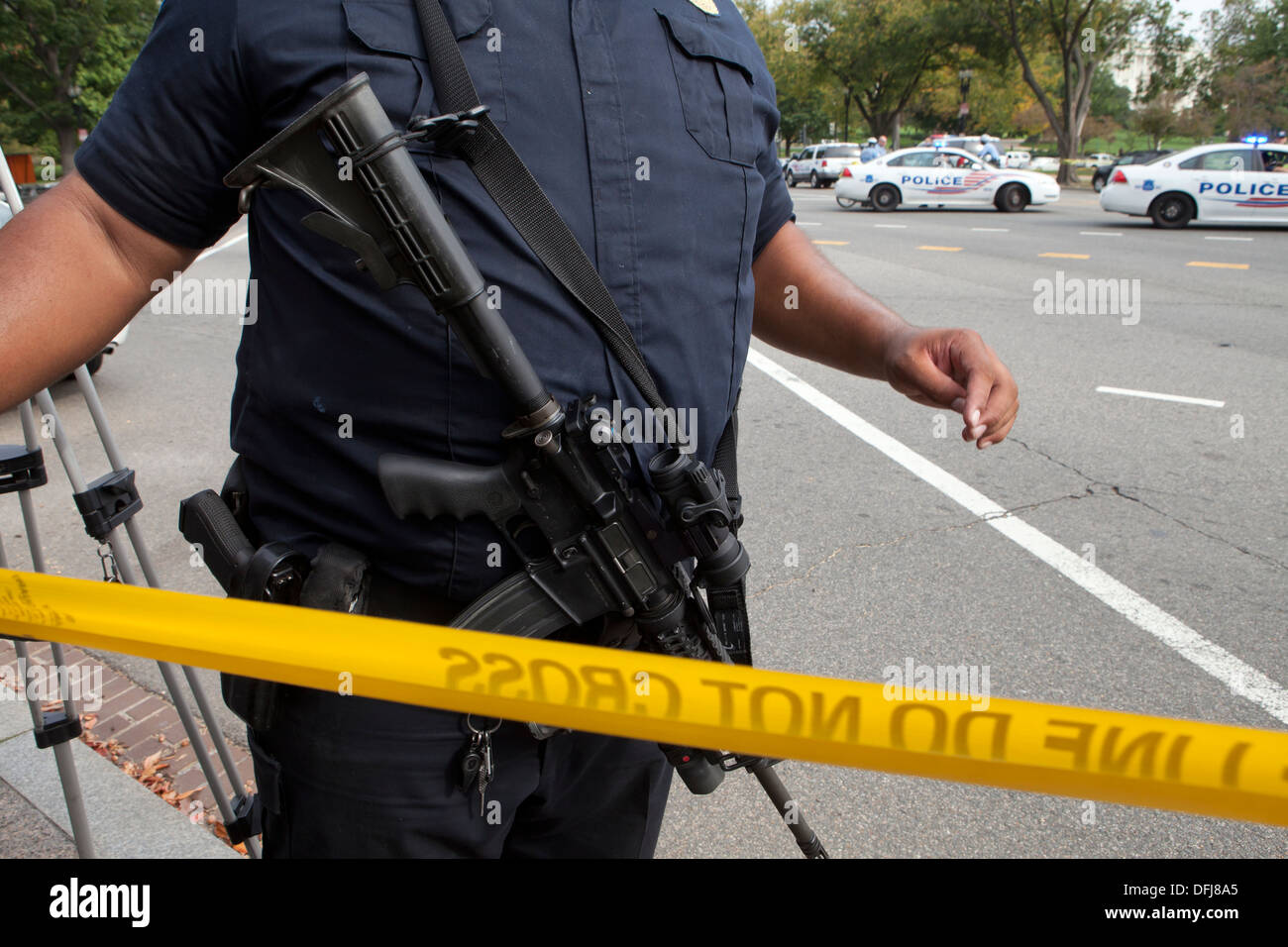 Policeman carrying a semi-auto rifle putting up police line tape at a crime scene - Washington, DC USA Stock Photo