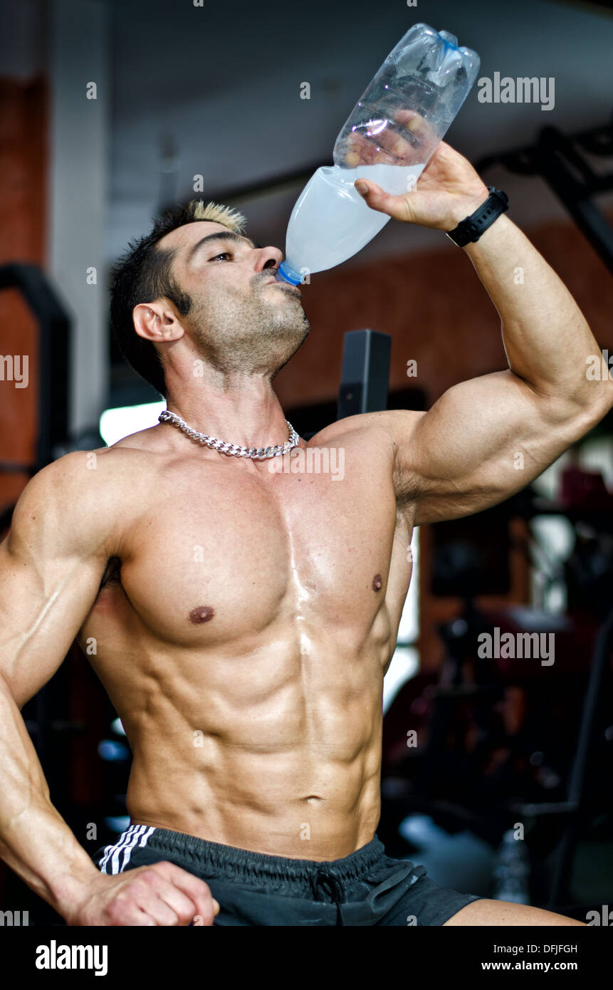 Muscular male bodybuilder in a gym drinking water or energy drink from
