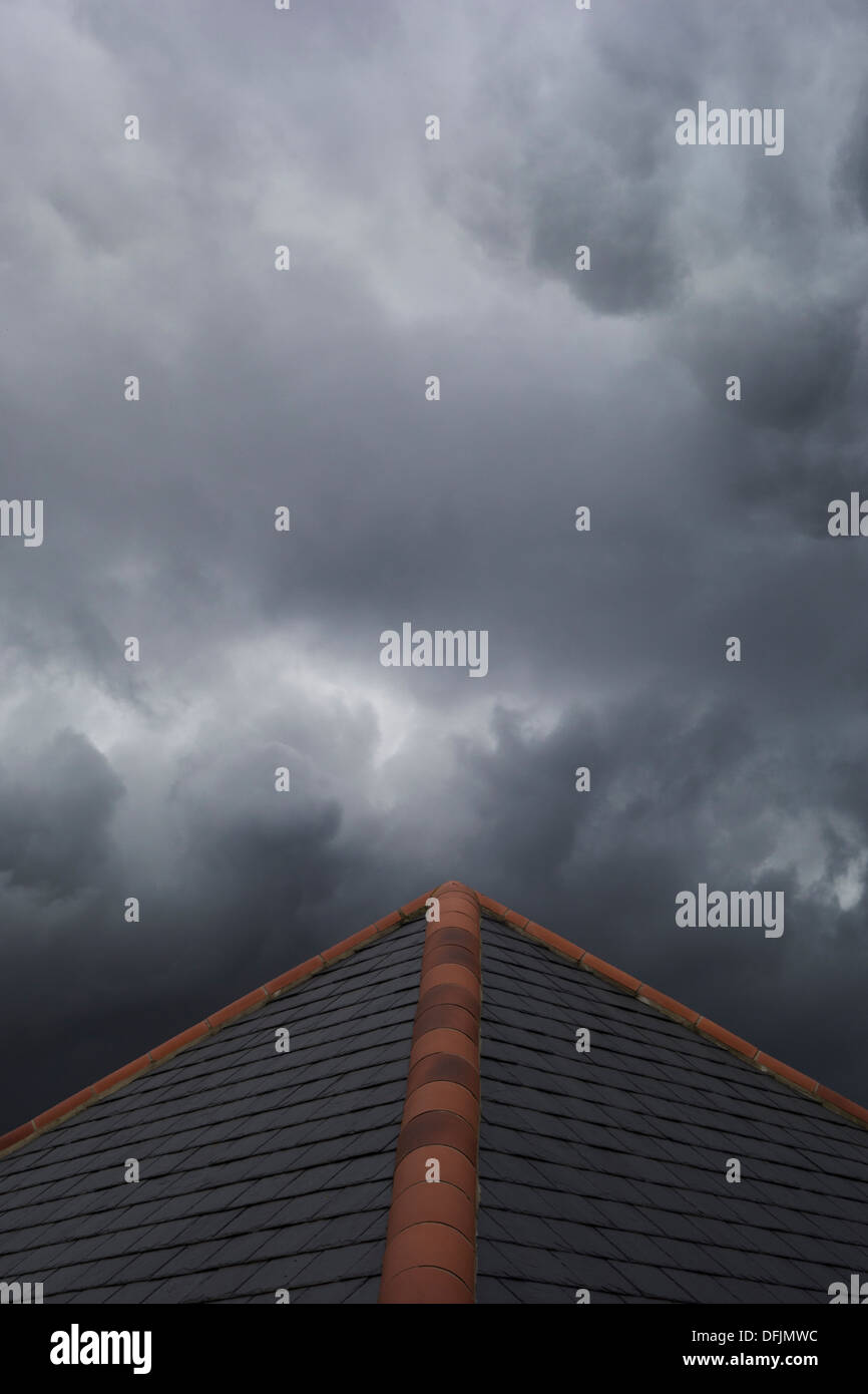 Dark stormy clouds gathering above a tiled roof. Stock Photo
