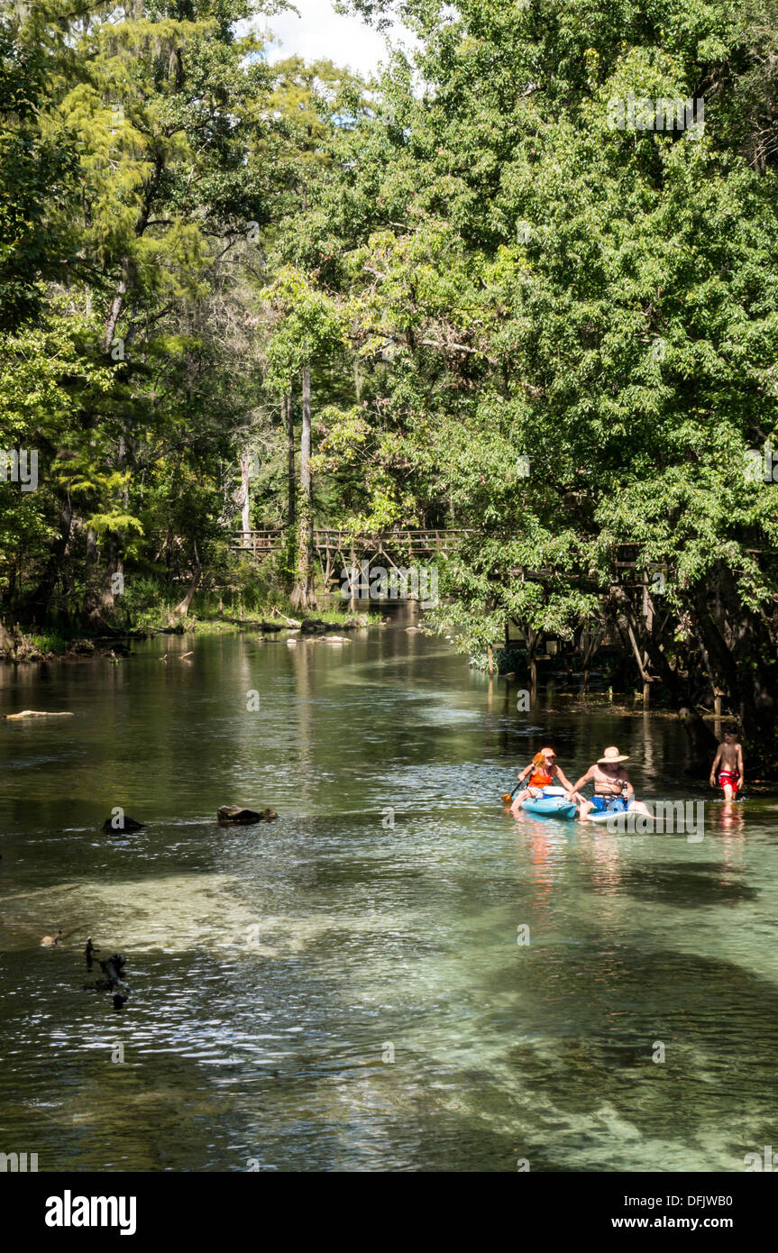 Man and woman in kayak and surf board with young preteen boy wearing red swim trunks wading in shallow, clear spring run water. Stock Photo