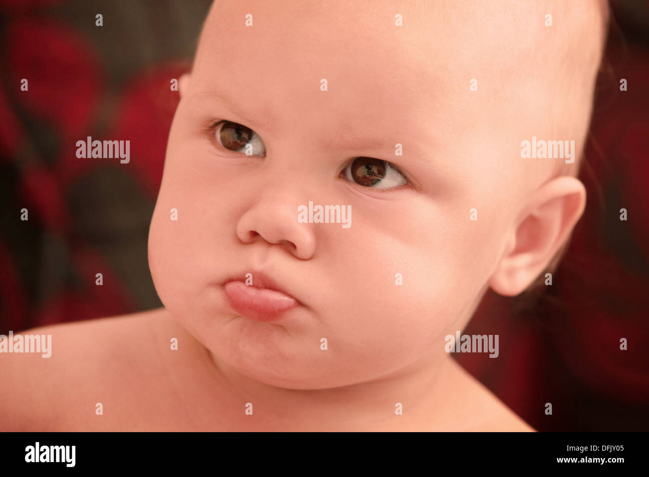 Funny angry Caucasian baby girl close-up portrait on dark blurred background Stock Photo