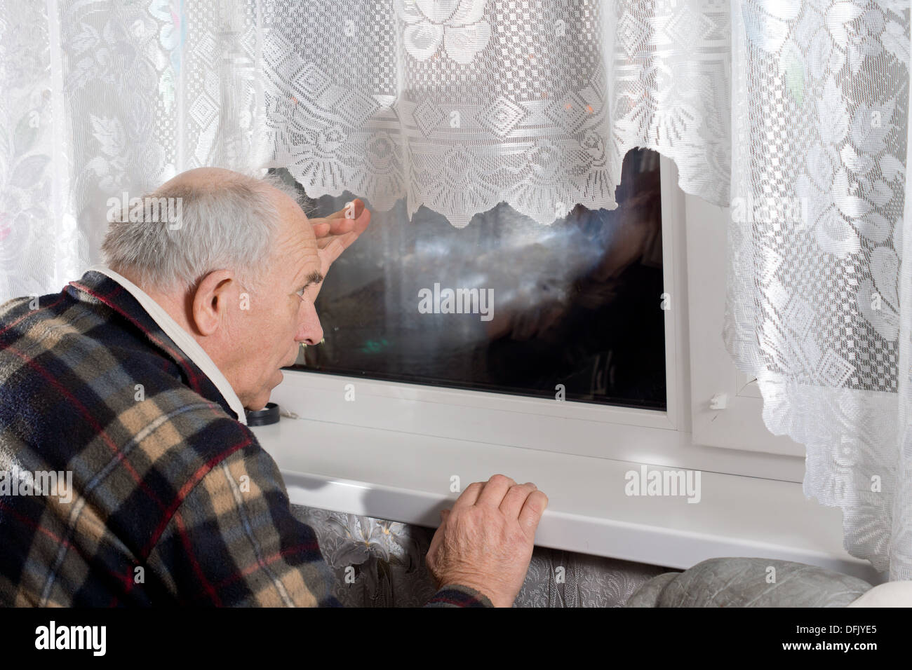 Senior man peering through a window at night as he watches for someone to arrive Stock Photo