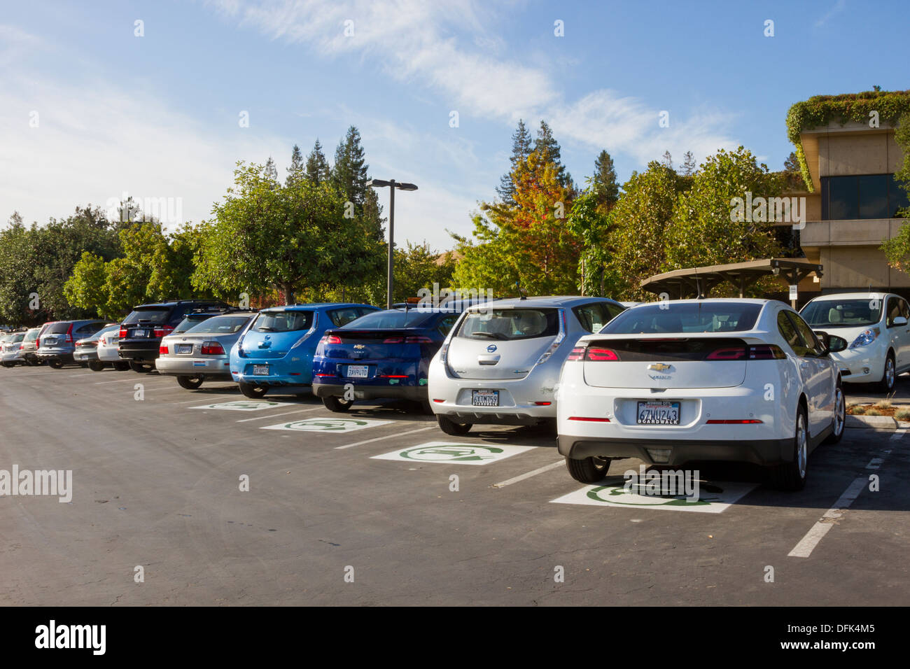 Plug-in electric cars parked in parking spaces reserved for EV cars at a company parking lot Stock Photo