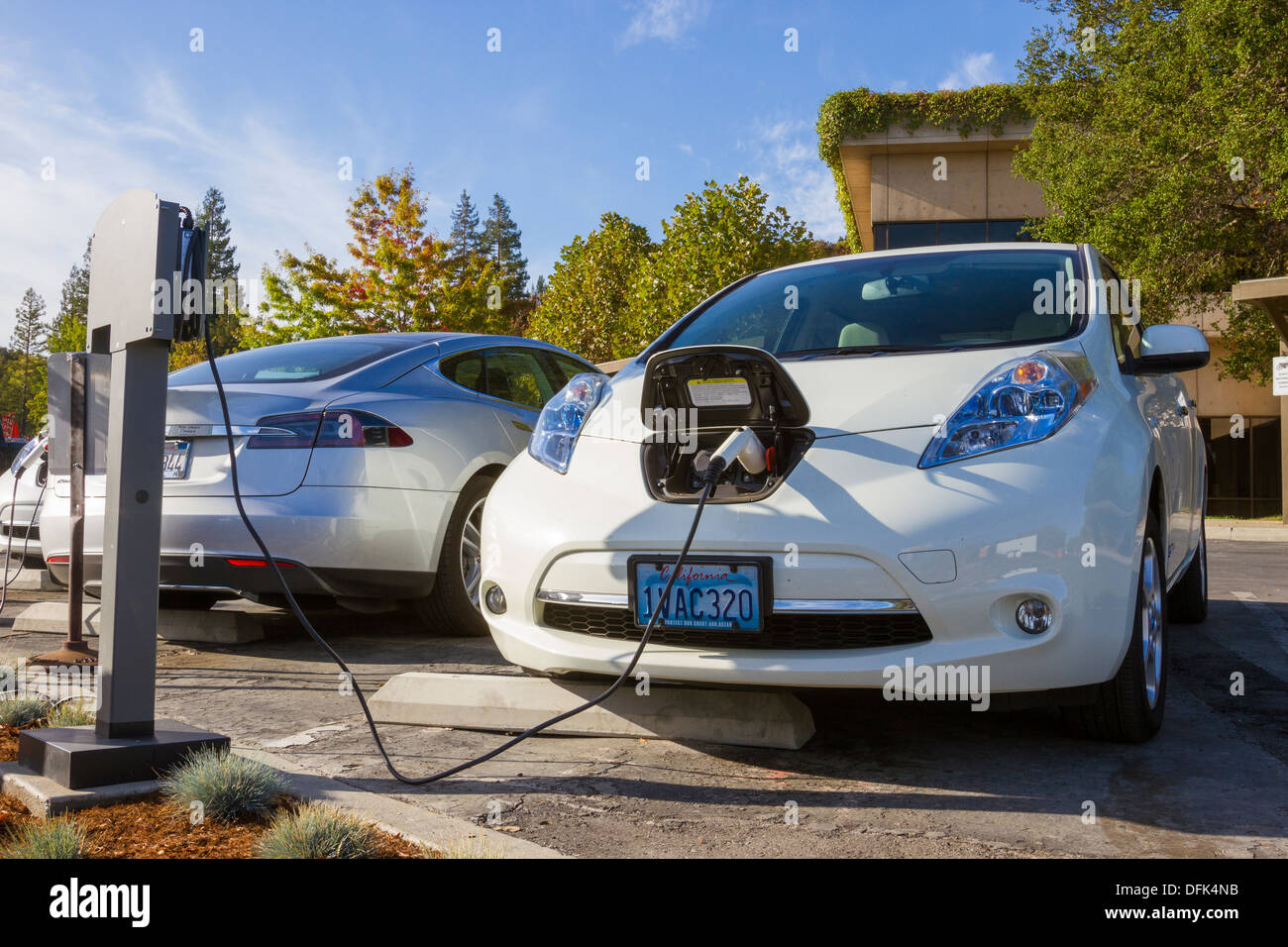 Nissan Leaf plug-in electric car parked in an EV parking spot at work and plugged into a charging station Stock Photo