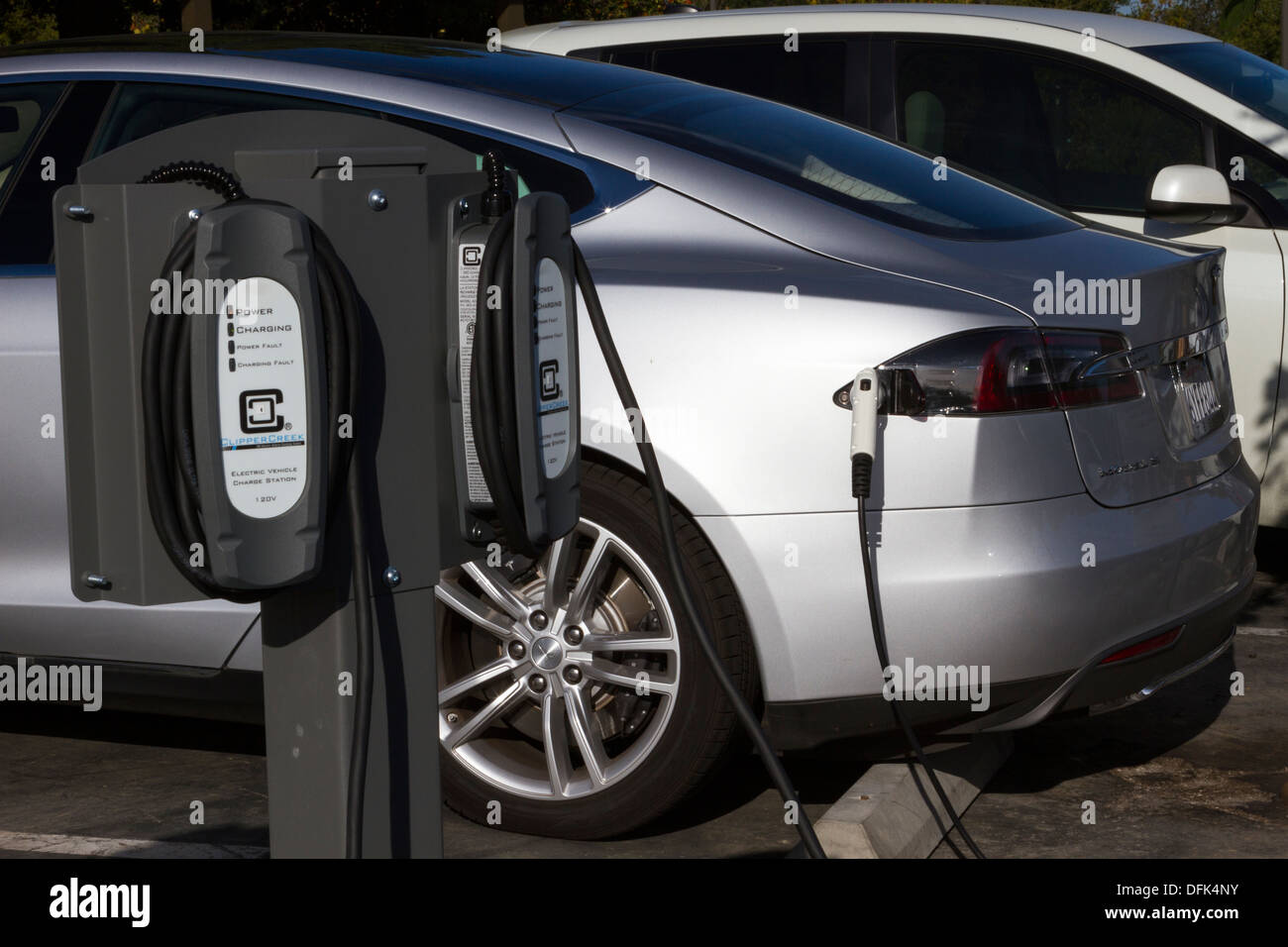 Tesla Model S plug-in electric car plugged into a charging station in a company parking lot Stock Photo