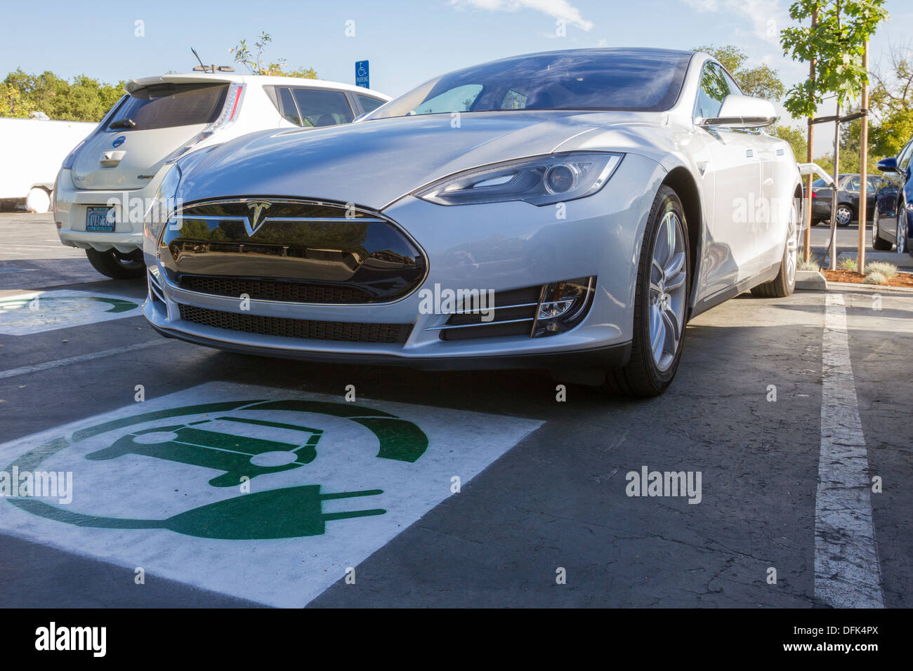 Tesla Model S plug-in electric car parked in a parking spot with EV symbol and plugged into a charging station at work Stock Photo