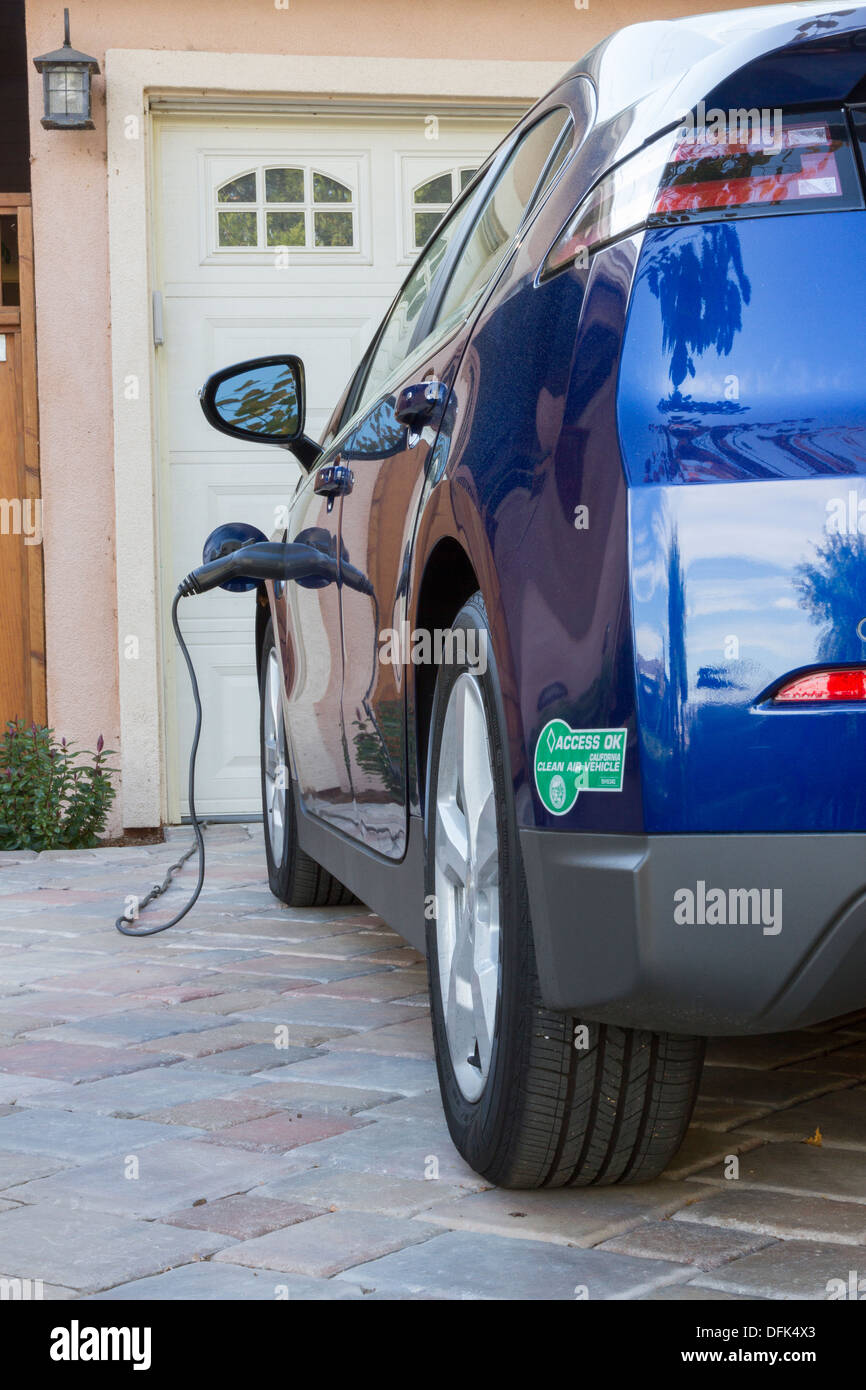 Plug-in electric car with carpool sticker parked in driveway, with connector plugged in and charging at home Stock Photo