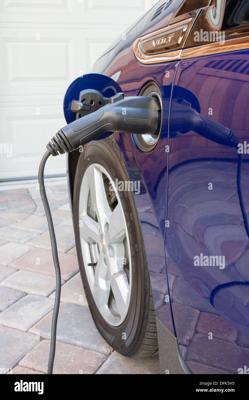 Plug-in electric car with connector plugged in charging, parked at home in a driveway Stock Photo