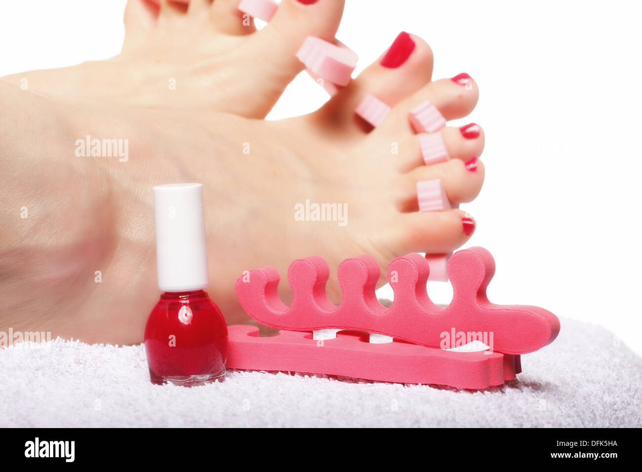foot pedicure applying woman's feet with red toenails in toe separators ...