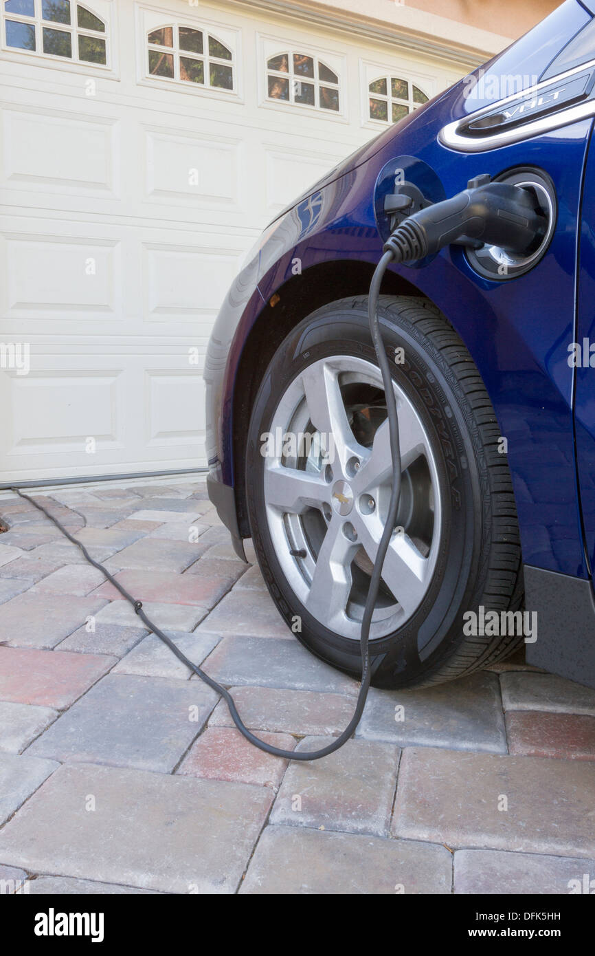 Chevrolet Volt plug-in hybrid electric car with connector plugged in and charging, parked at home in a driveway Stock Photo